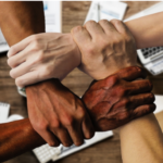 Four hands from varying ethnic backgrounds grip to illustrate inclusion.